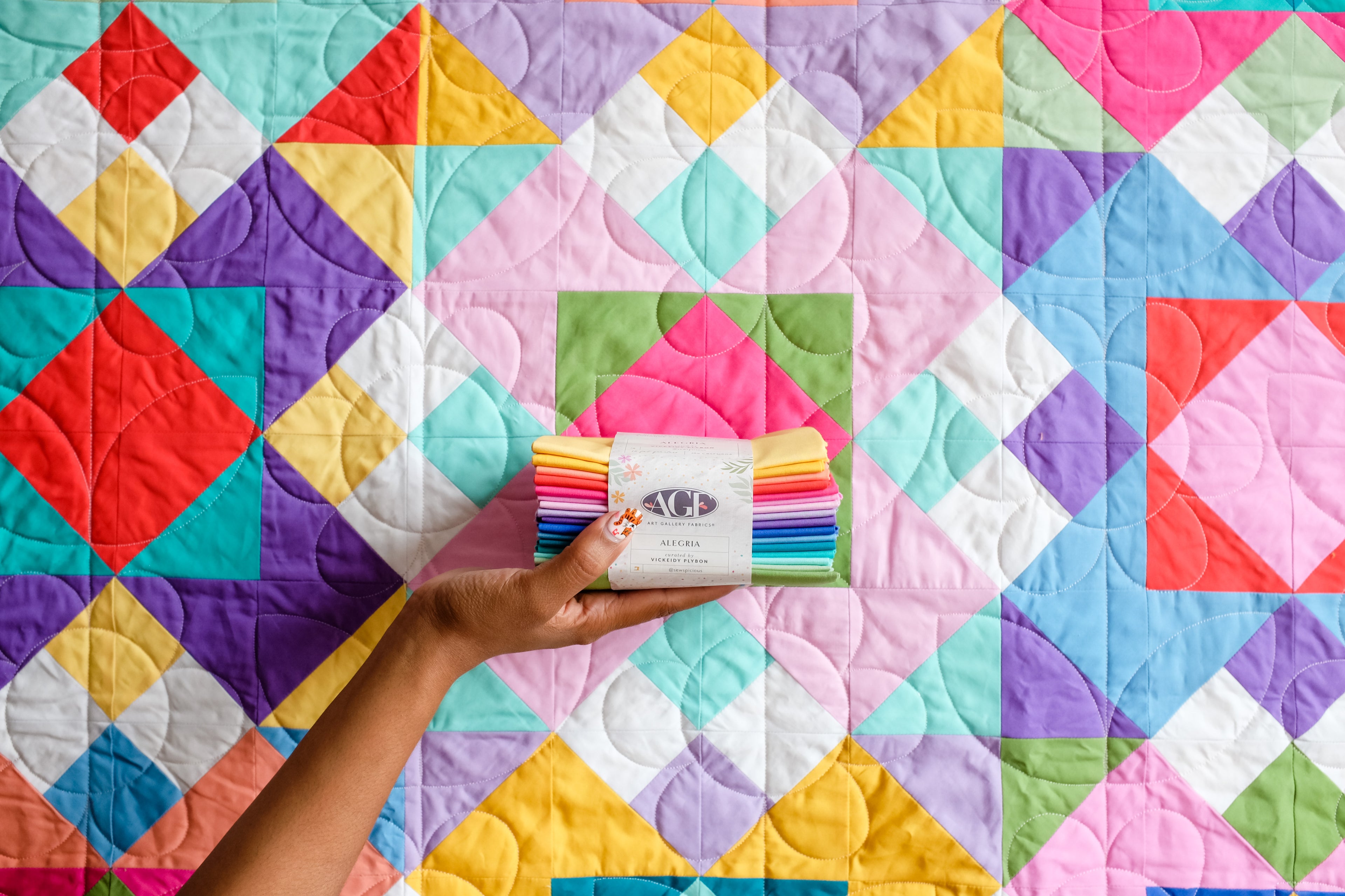 Hand Holding bundle of fabric in front of a colorful quilt