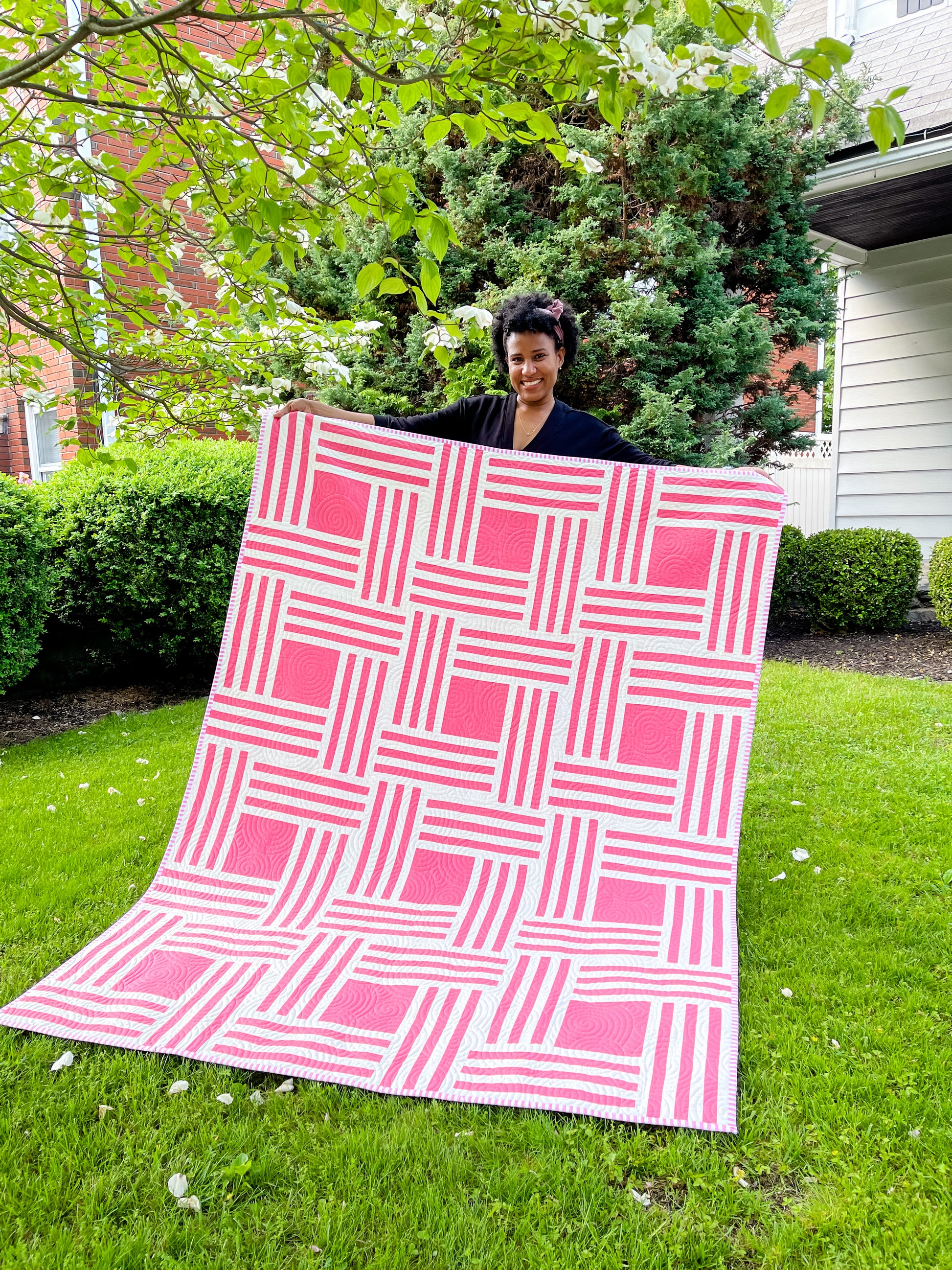 Person holding quilt with pink and white strips and pink squares. 