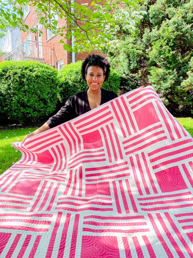 Person holding quilt pink and white stripes with pink squares in the middle. 