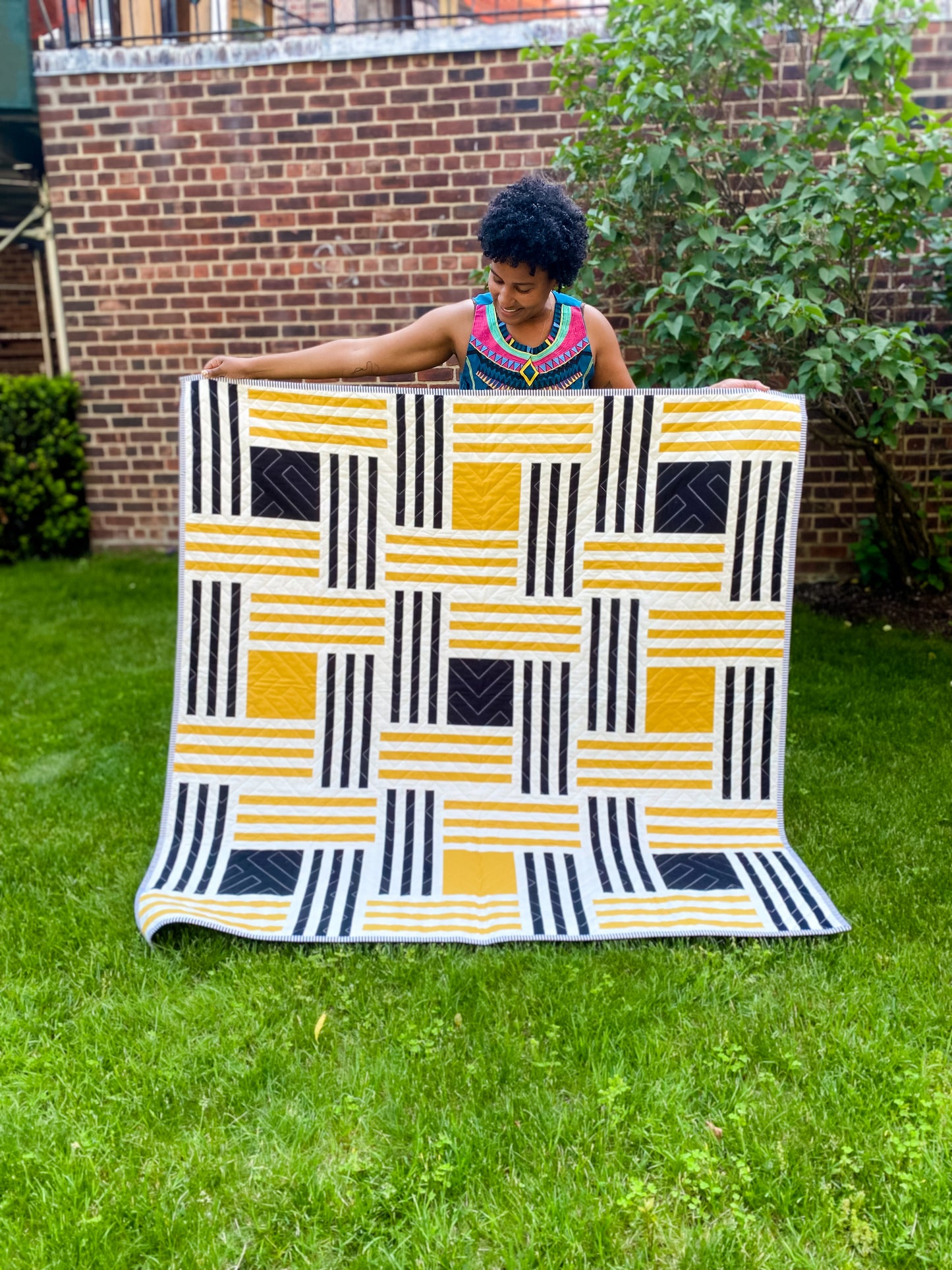 Person holding quilt with white, black and yellow stripes and alternating black and yellow squares in the middle
